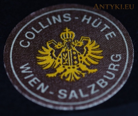 Zbliżenie etykiety Collins-Hüte Wien-Salzburg ze złotym godłem