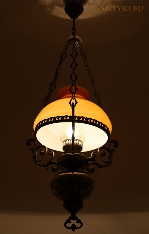 zapalona lampa z jasnym wnętrzem klosza i ozdobnymi mosiężnymi ramionami